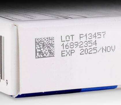 CIJ product marking: 2D code followed by three-line alpha-numeric text in black ink on coated paperboard